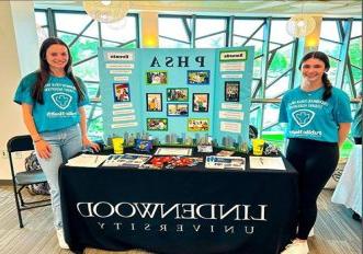 Two St. 路易斯公共卫生学位的学生穿着蓝绿色的衬衫站在桌子上展示他们的学位课程